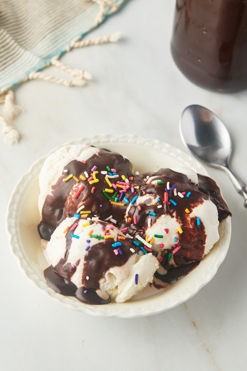 overhead view of a bowl of vanilla ice cream topped with hot fudge sauce and sprinkles