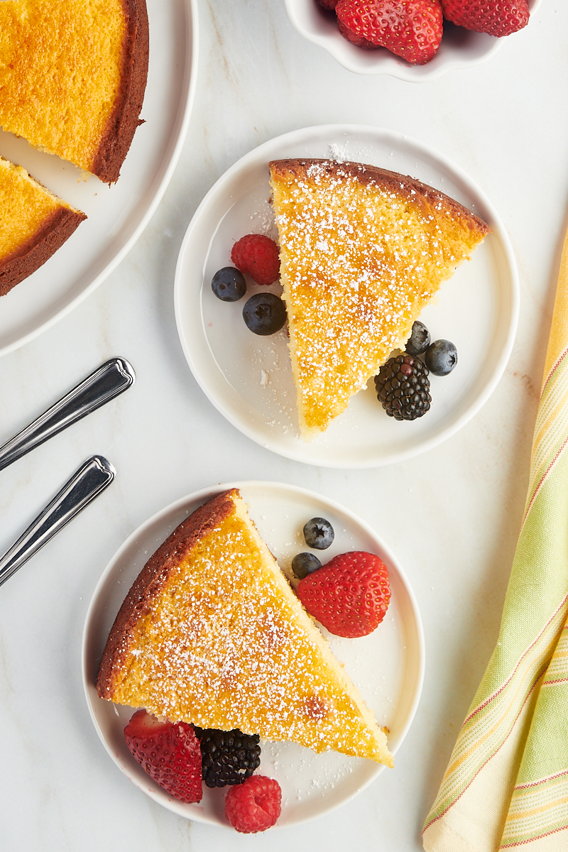 overhead view of two slices of lemon ricotta cake on white plates with fresh berries