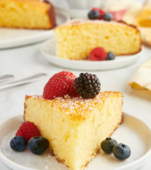 a slice of lemon ricotta cake served with fresh berries on a white plate