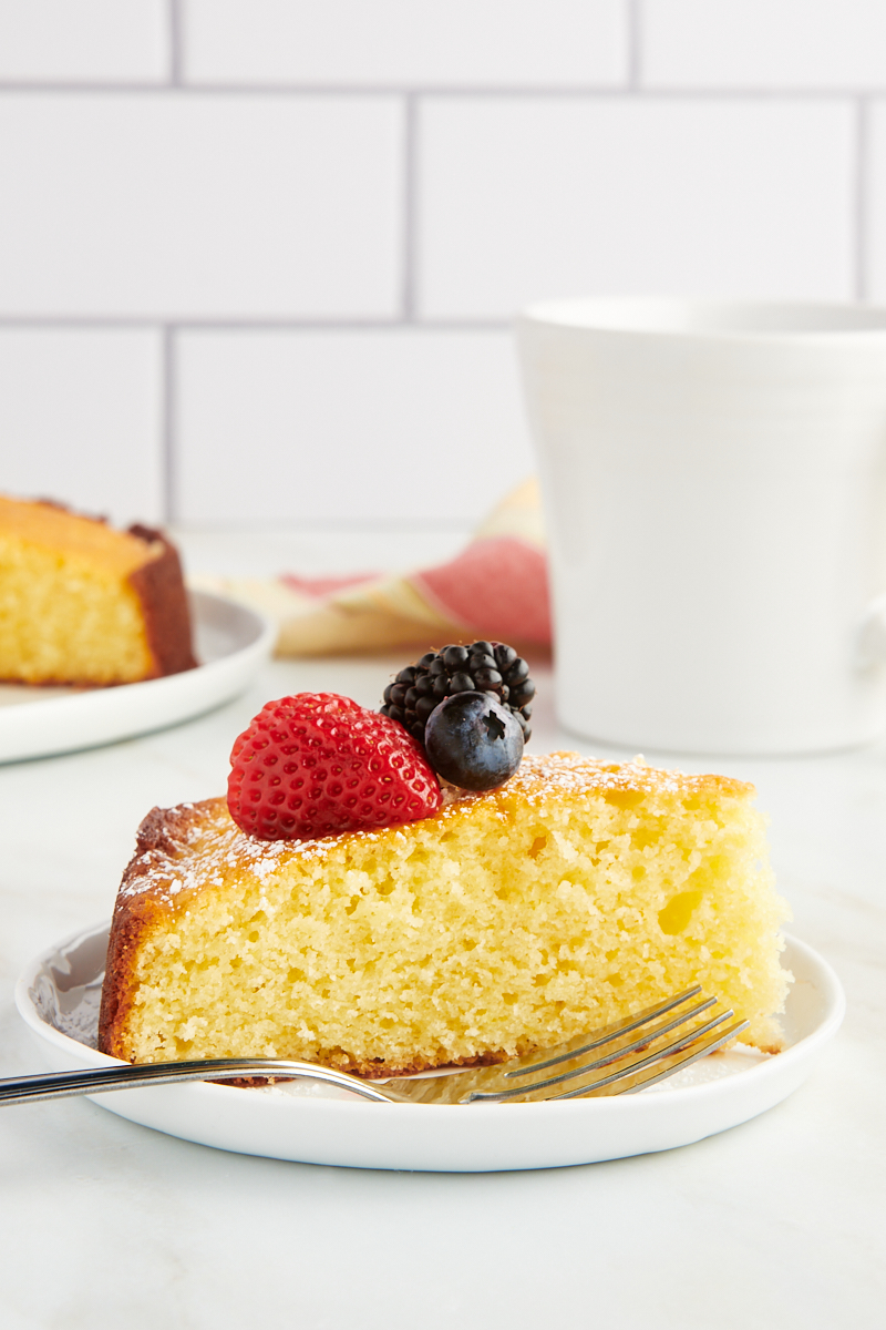 a slice of lemon ricotta cake topped with fresh berries served on a white plate