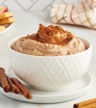 snickerdoodle cookie dip in a white bowl on a white plate with pretzels alongside
