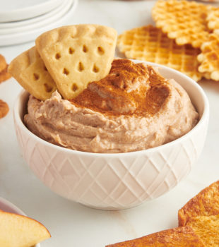 snickerdoodle cookie dip in a white bowl with two shortbread cookies sticking into it