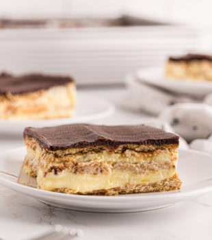 a slice of chocolate eclair cake on a white plate with more servings in the background