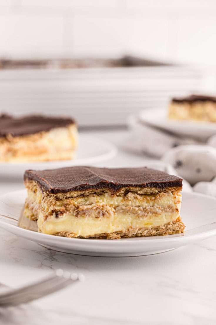 a slice of chocolate eclair cake on a white plate with more servings in the background