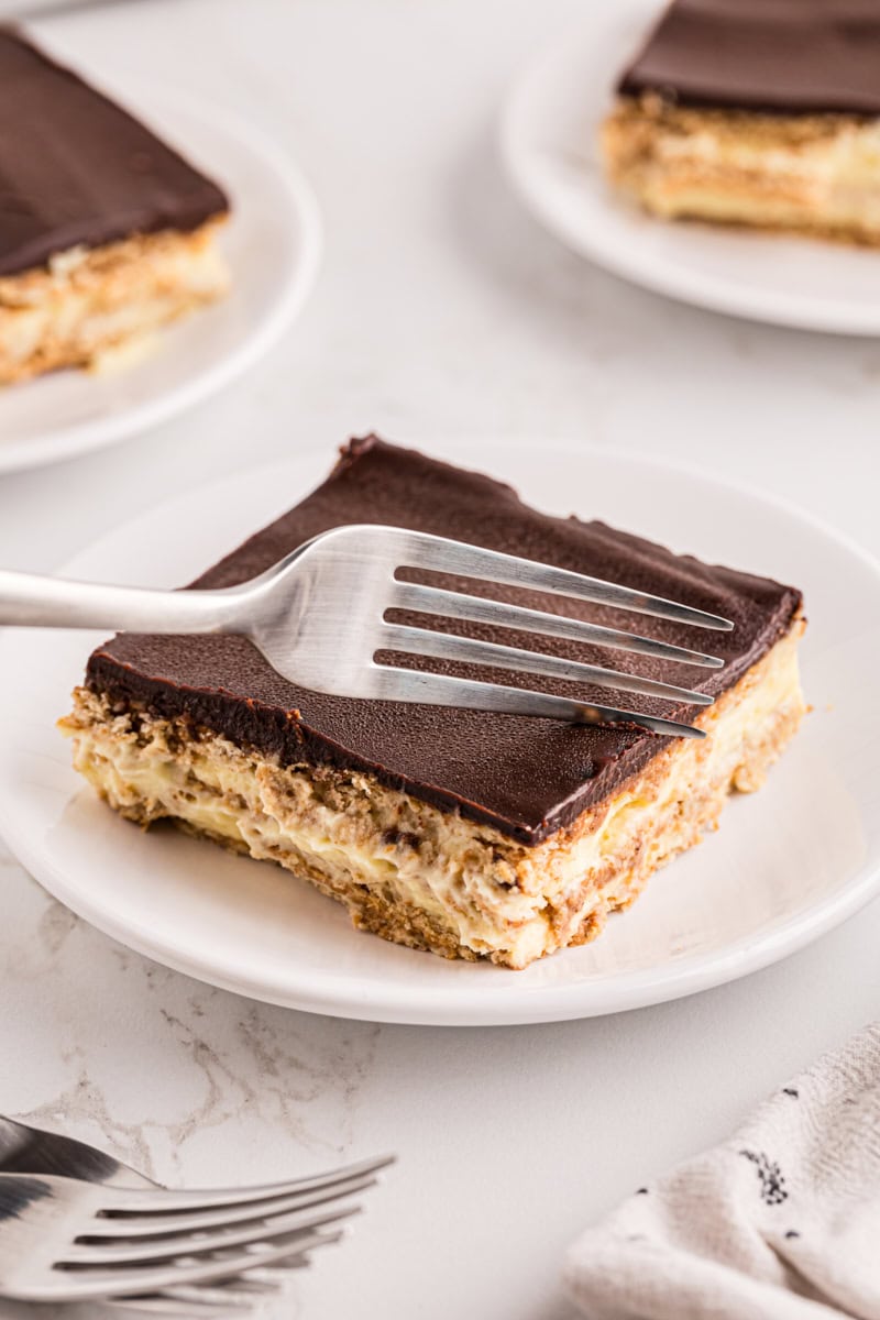 a fork cutting into a slice of chocolate eclair cake on a white plate
