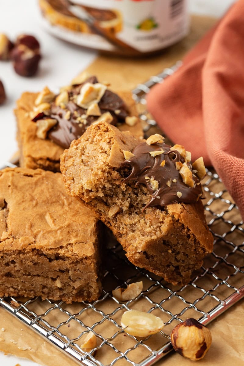 a hazelnut blondie with a bite missing leaned against two more blondies on a wire rack