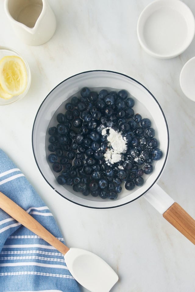 overhead view of blueberries, sugar, cornstarch, and lemon juice in a white saucepan