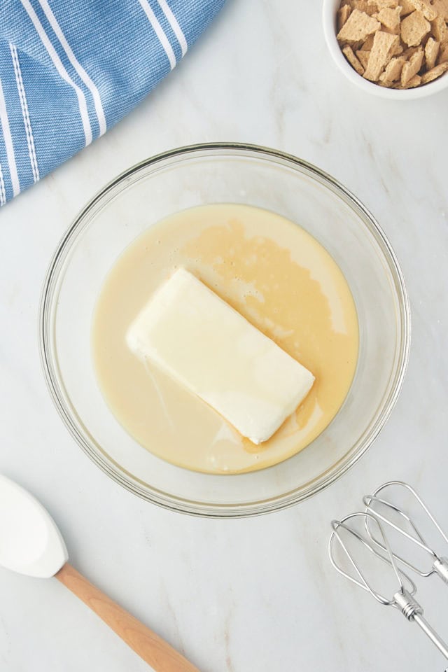 overhead view of cream cheese, sweetened condensed milk, and vanilla extract in a glass mixing bowl
