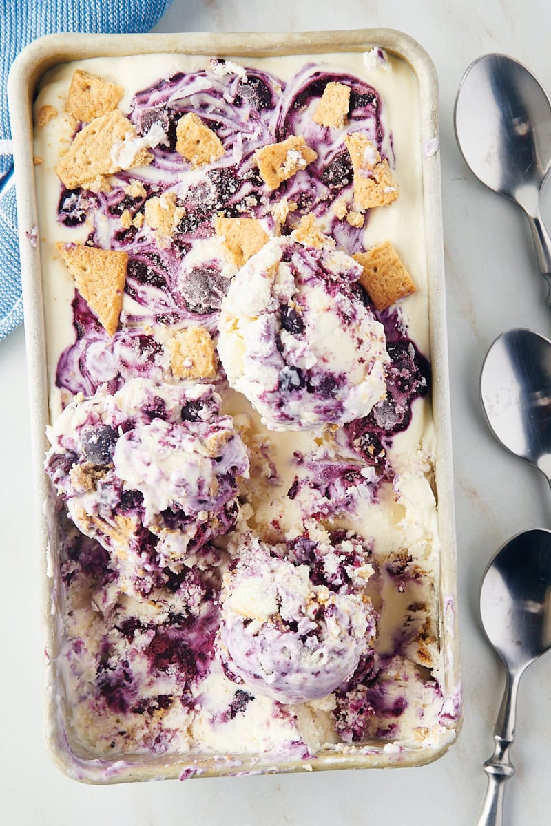 overhead view of scoops of blueberry cheesecake ice cream on top of the remaining ice cream in a metal loaf pan