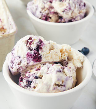 a bowl of blueberry cheesecake ice cream with another bowl of ice cream in the background