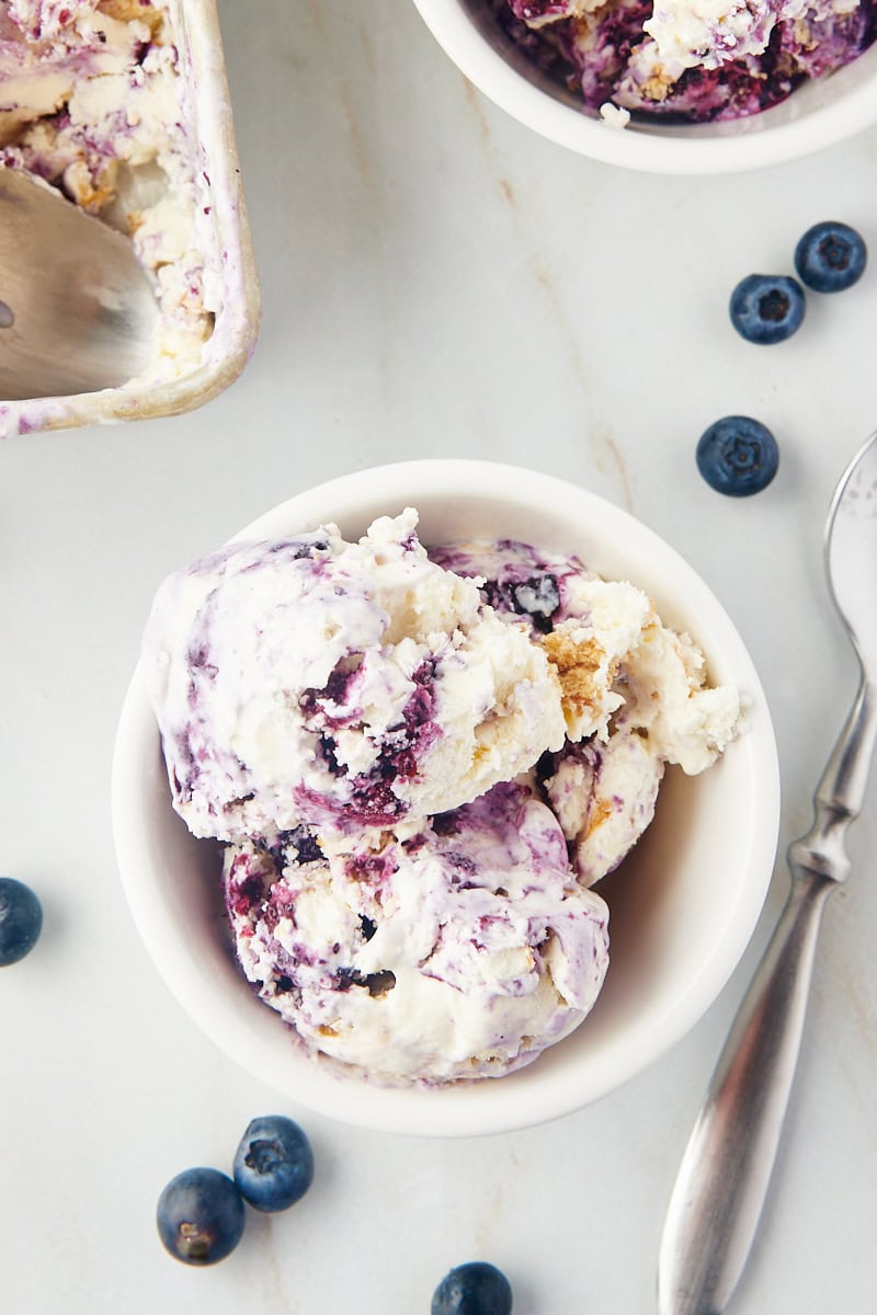 overhead view of blueberry cheesecake ice cream in a white bowl with blueberries scattered around the bowl