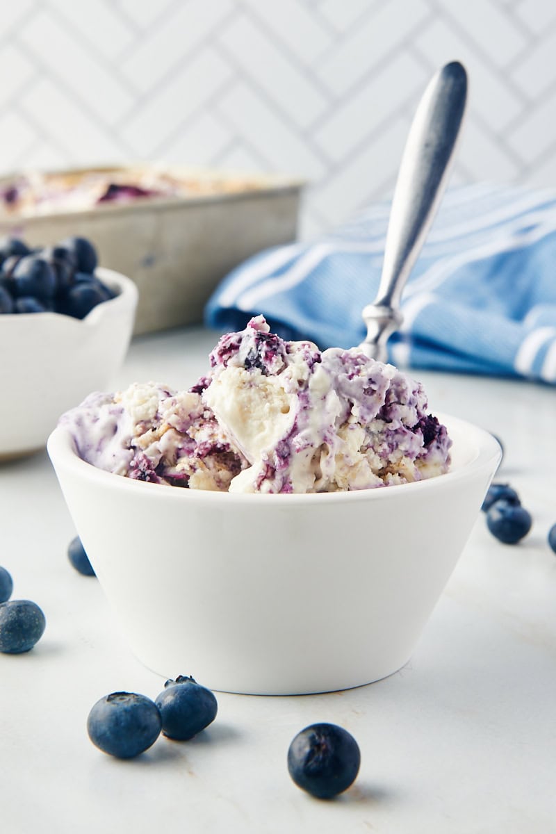blueberry cheesecake ice cream in a white bowl with more ice cream and blueberries in the background