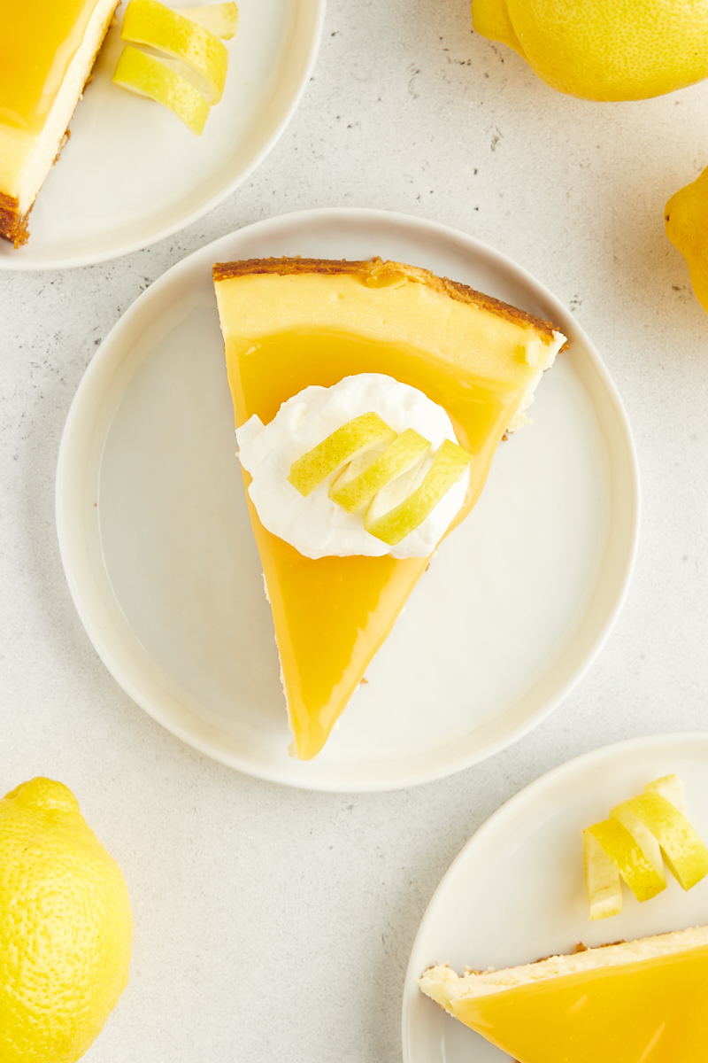 overhead view of a slice of lemon cheesecake topped with lemon curd, whipped cream, and a lemon curl
