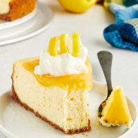 a slice of lemon cheesecake on a white plate with a bite on a fork
