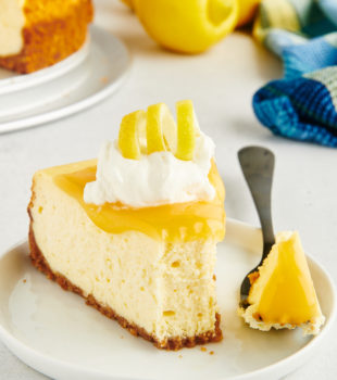 a slice of lemon cheesecake on a white plate with a bite on a fork