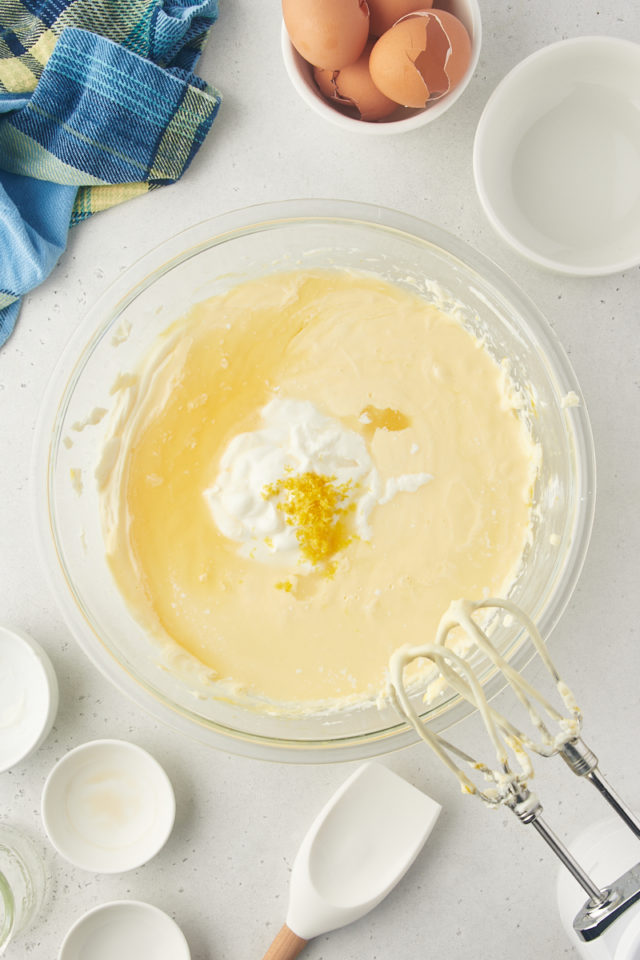 overhead view of sour cream, lemon juice, lemon zest, vanilla extract, and lemon extract added to lemon cheesecake batter