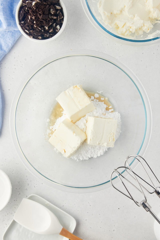 overhead view of cream cheese, confectioners' sugar, and vanilla extract in a glass mixing bowl