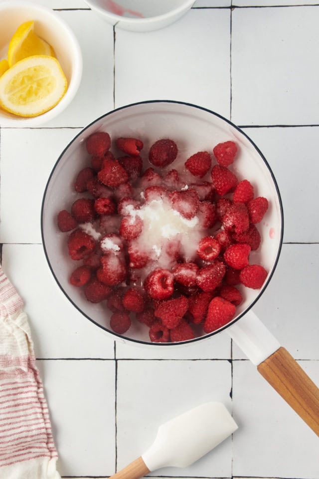 overhead view of raspberries, sugar, and lemon juice in a saucepan