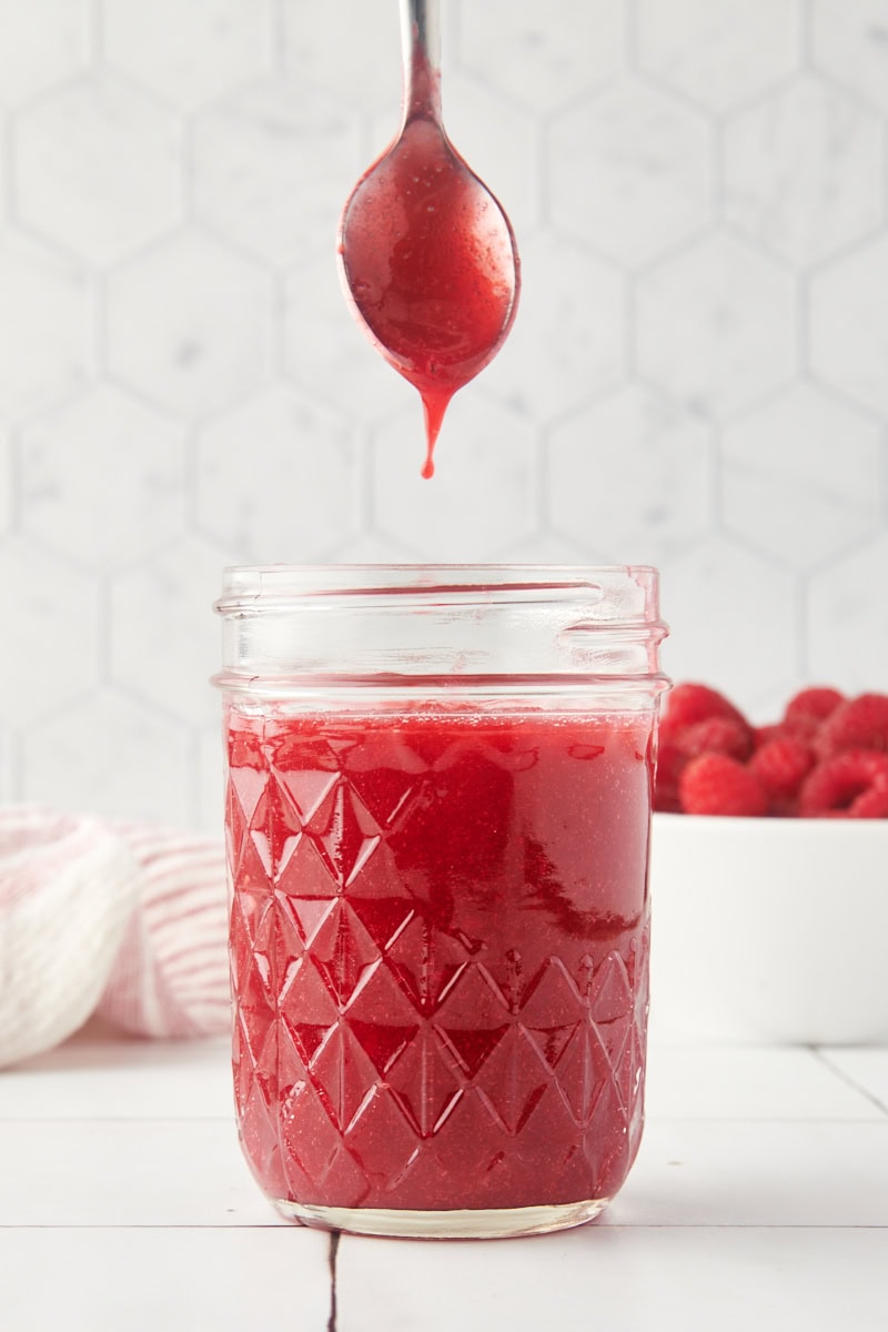 a spoonful of raspberry coulis lifting up from a glass jar of more sauce