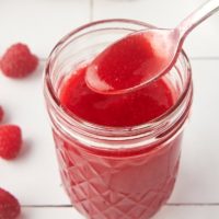 a jar of raspberry coulis with a spoonful held over the top