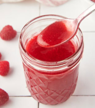 a jar of raspberry coulis with a spoonful held over the top