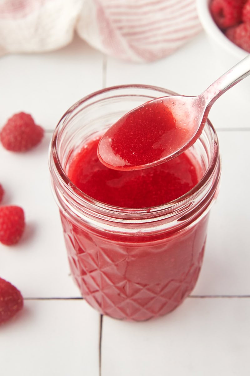 a jar of raspberry coulis with a spoonful held over the top