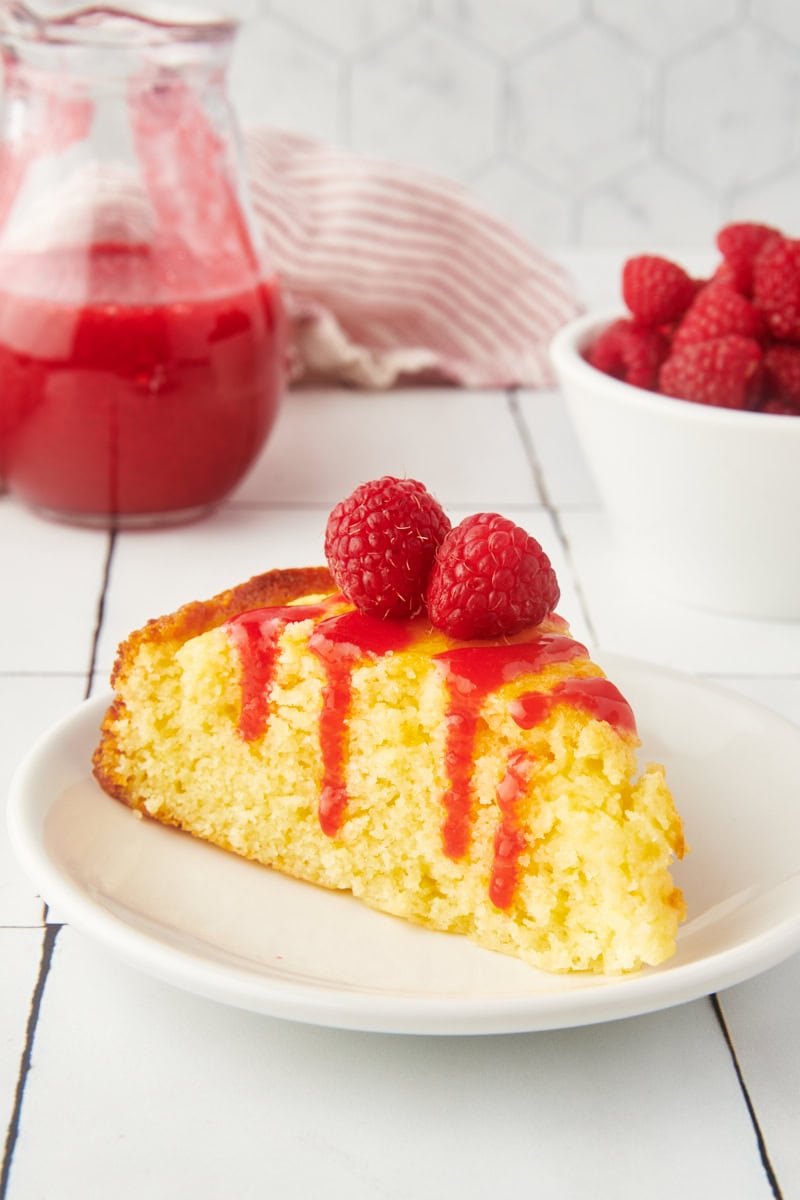 a slice of ricotta cake topped with raspberry coulis and fresh raspberries