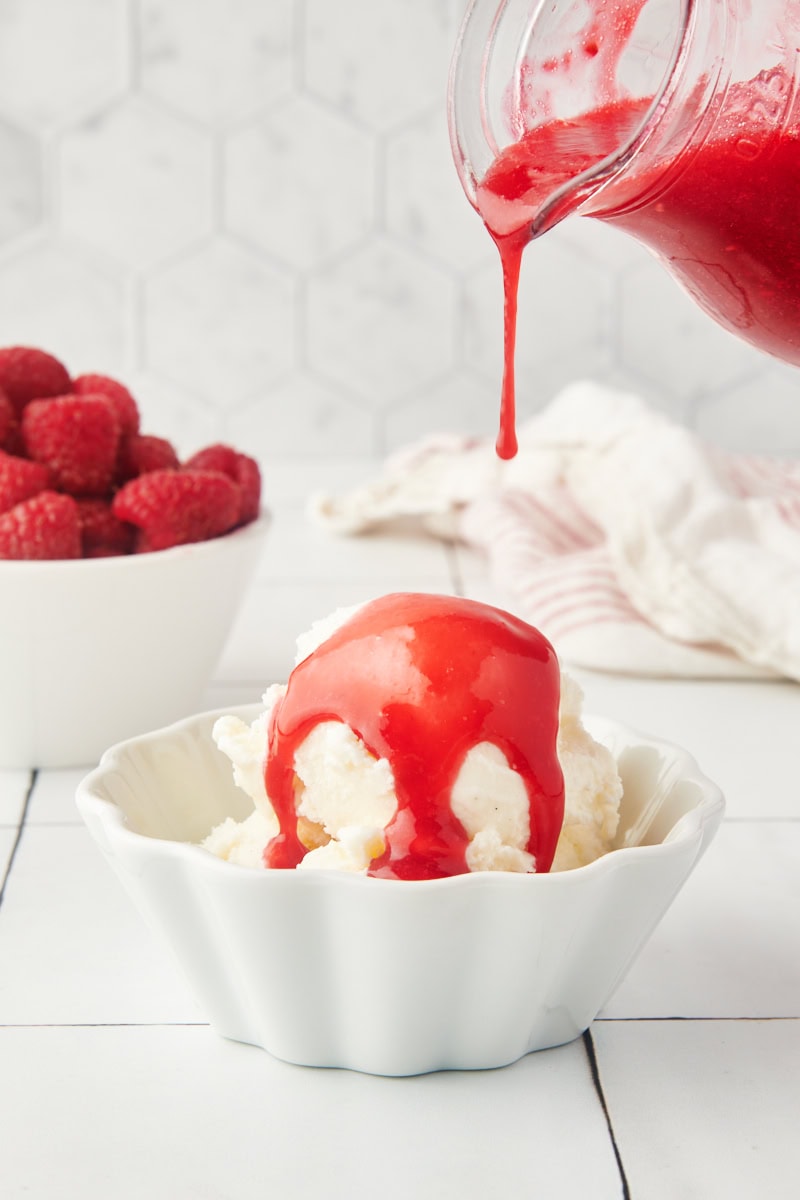 raspberry coulis pouring over ice cream in a white bowl