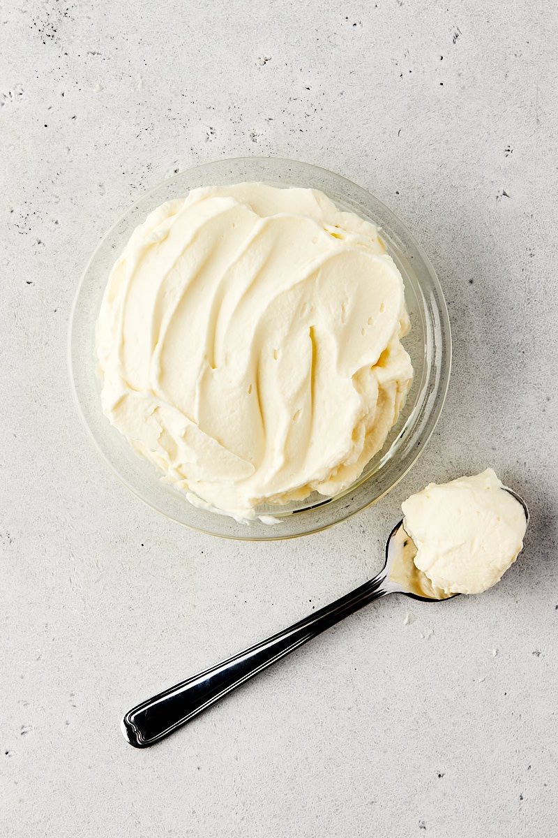 overhead view of stabilized whipped cream in a glass bowl with more on a spoon alongside