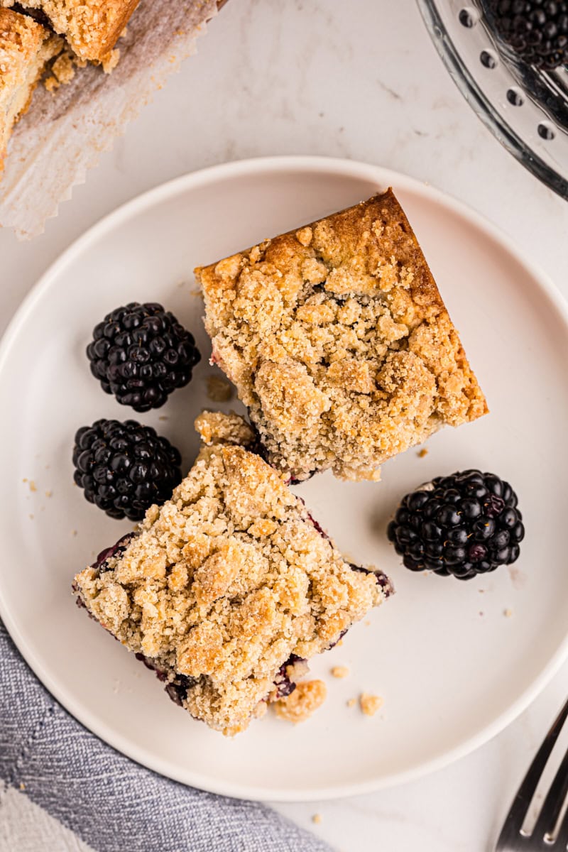 overhead view of two blackberry crumb bars and three blackberries on a white plate