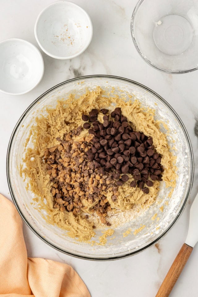 overhead view of chocolate chips and toffee bits added to blondie batter in a glass mixing bowl