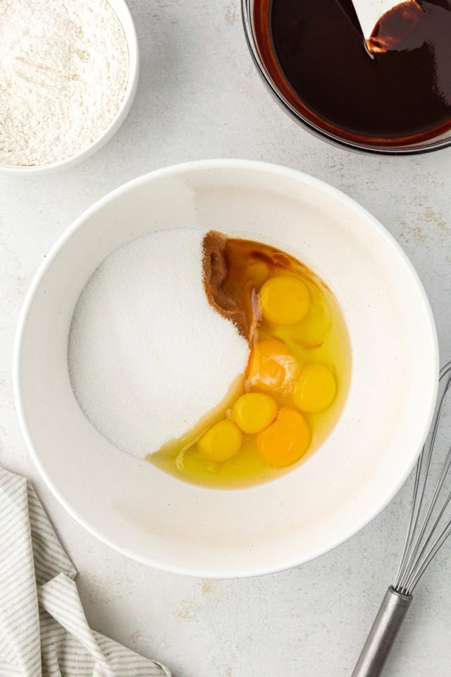 overhead view of sugar, eggs, and vanilla in a white mixing bowl