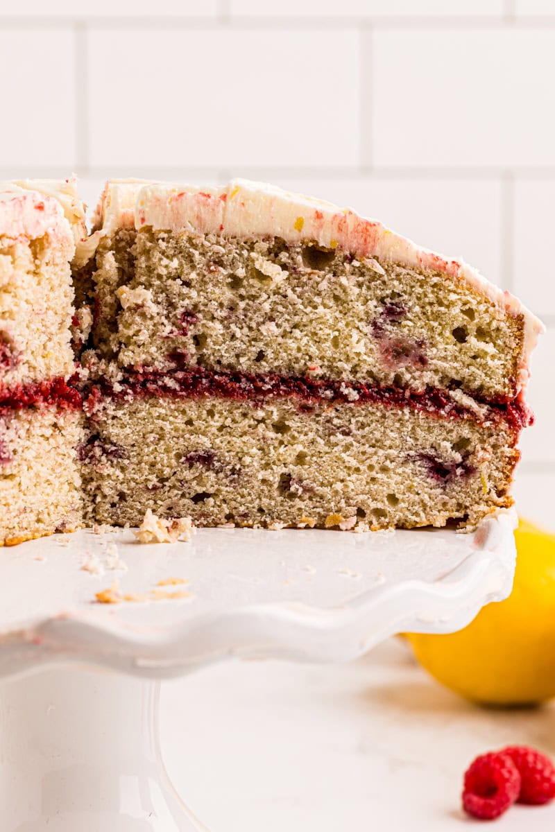 partially sliced lemon raspberry cake on a white cake stand