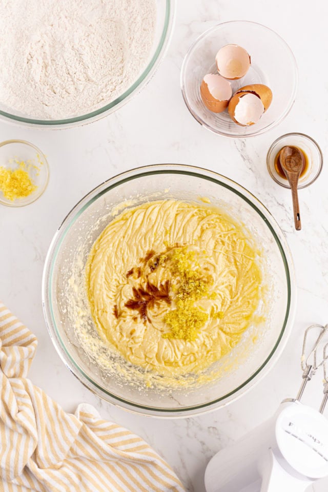 overhead view of vanilla extract and lemon zest added to cake batter in a glass mixing bowl