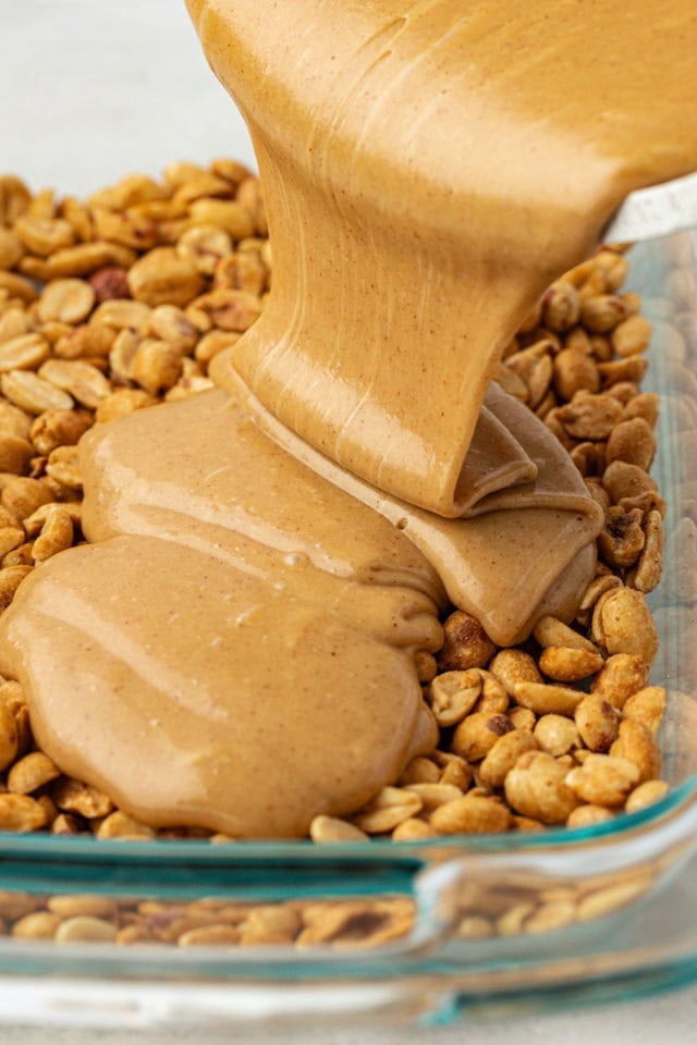 peanut butter filling pouring over peanuts in a glass pan
