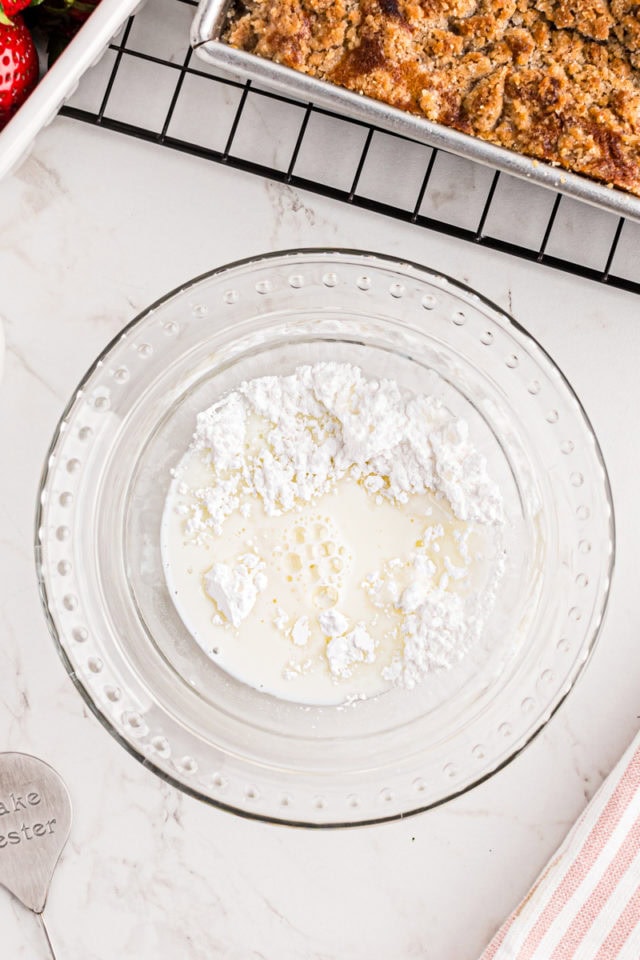 overhead view of confectioners' sugar, milk, and vanilla in a glass mixing bowl