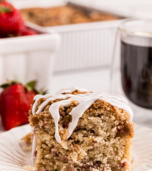 a slice of strawberry coffee cake on a white plate with berries and more cake in the background