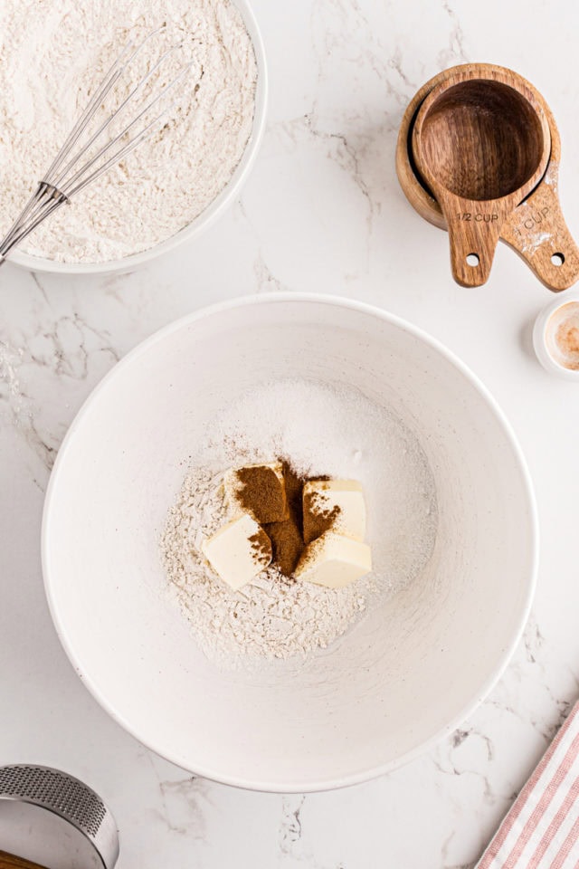 overhead view of butter added to flour, sugar, and cinnamon in a white mixing bowl