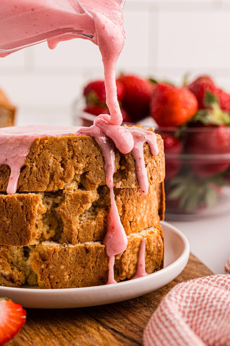 strawberry glaze pouring over a stack of three slices of strawberry pound cake on a white plate