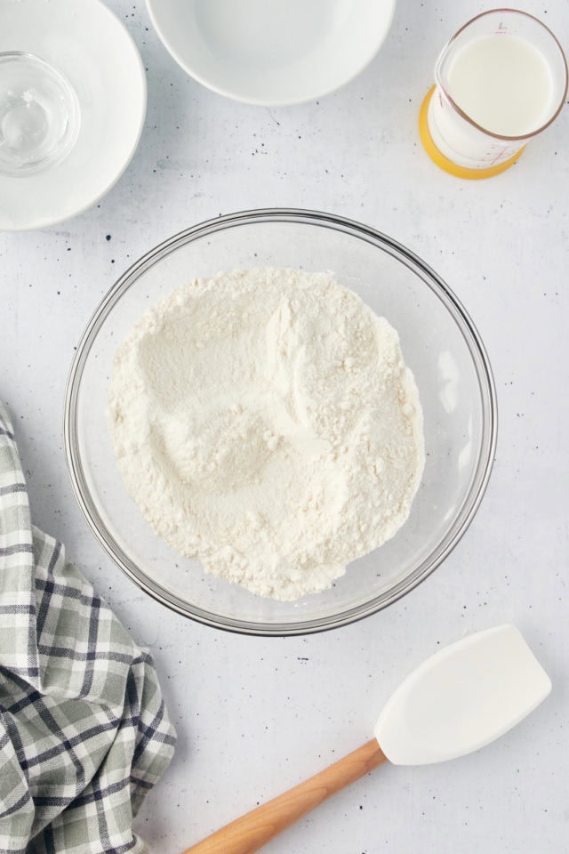 overhead view of flour, sugar, baking powder, and salt mixed in a glass mixing bowl