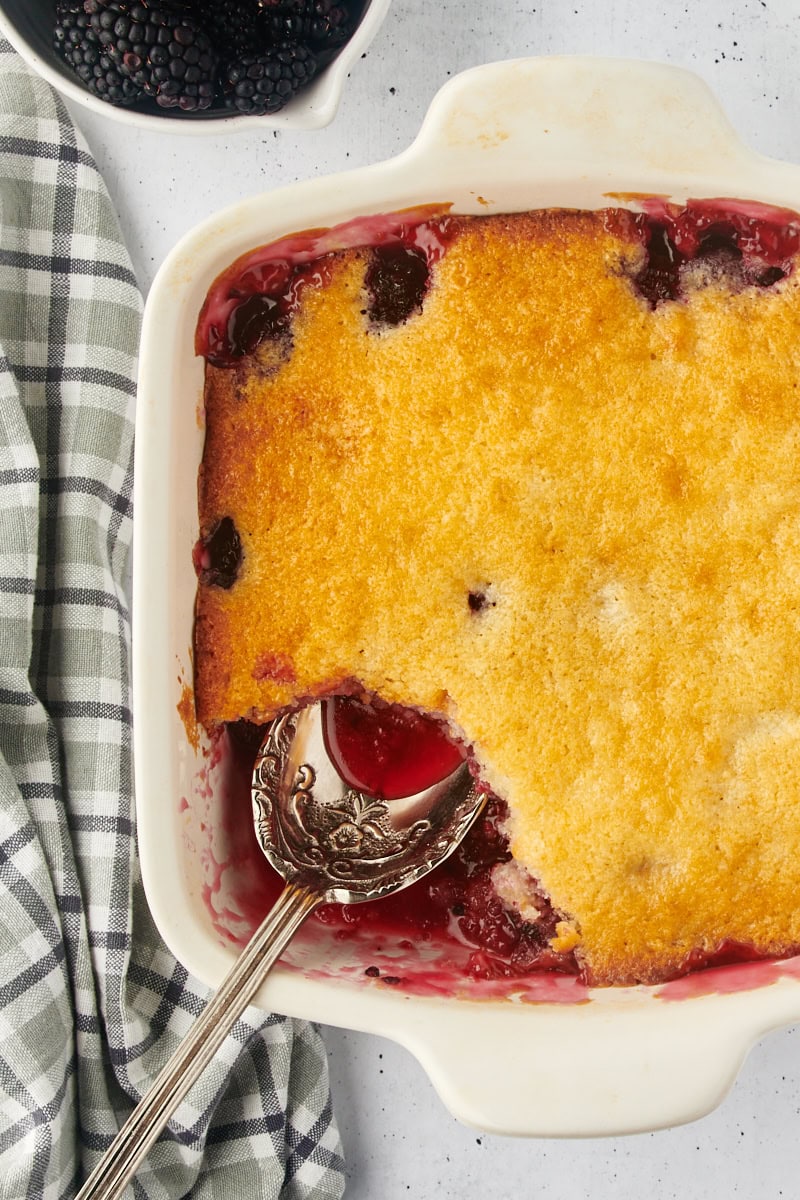 overhead view of blackberry cobbler with a spoon resting where a portion is missing