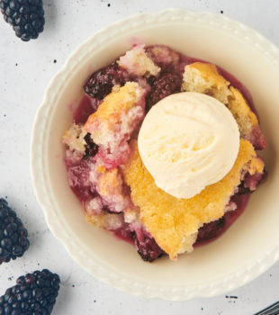 overhead view of blackberry cobbler topped with vanilla ice cream and served in a white bowl