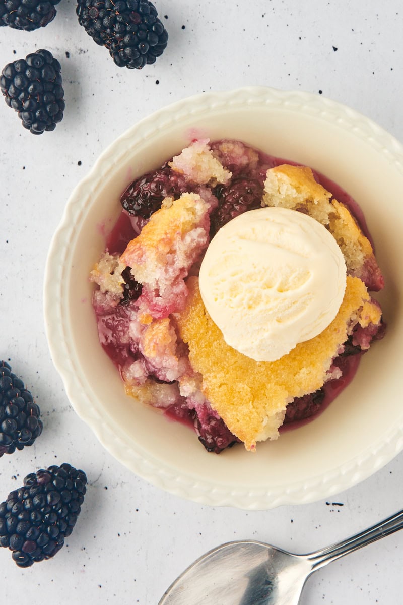 overhead view of blackberry cobbler topped with vanilla ice cream and served in a white bowl