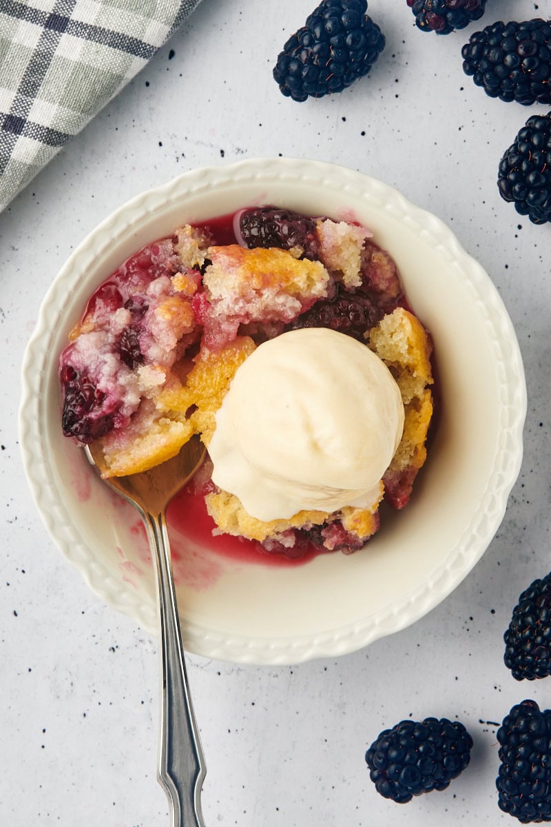 overhead view of blackberry cobbler topped with ice cream in a white bowl with a spoon sticking out of the bowl