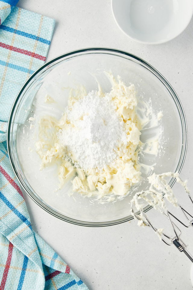 overhead view of cream cheese and confectioners' sugar in a glass mixing bowl