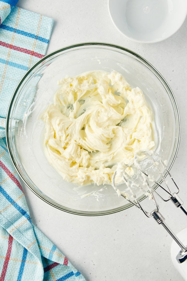 overhead view of beaten cream cheese and confectioners' sugar in a glass mixing bowl