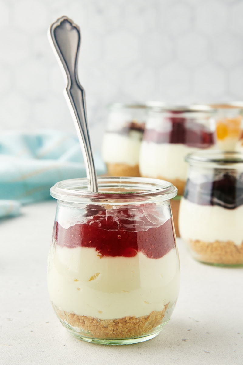 a no-bake cheesecake jar topped with cherry pie filling with more cheesecakes in the background