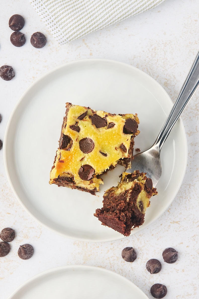 overhead view of a chocolate chip cheesecake brownies on a white plate with a bite on a fork