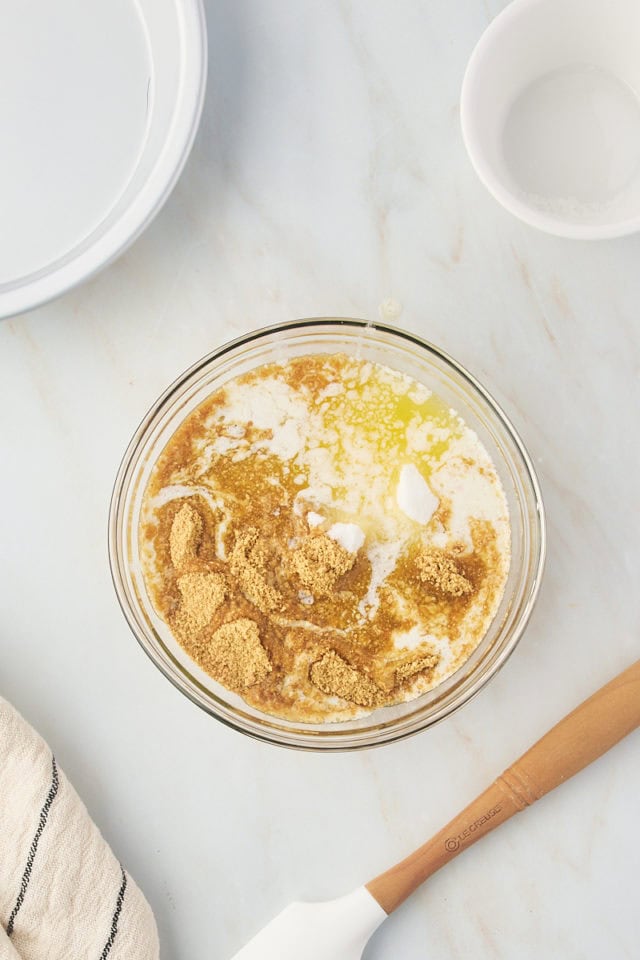 overhead view of graham cracker crumbs, melted butter, and sugar in a glass mixing bowl