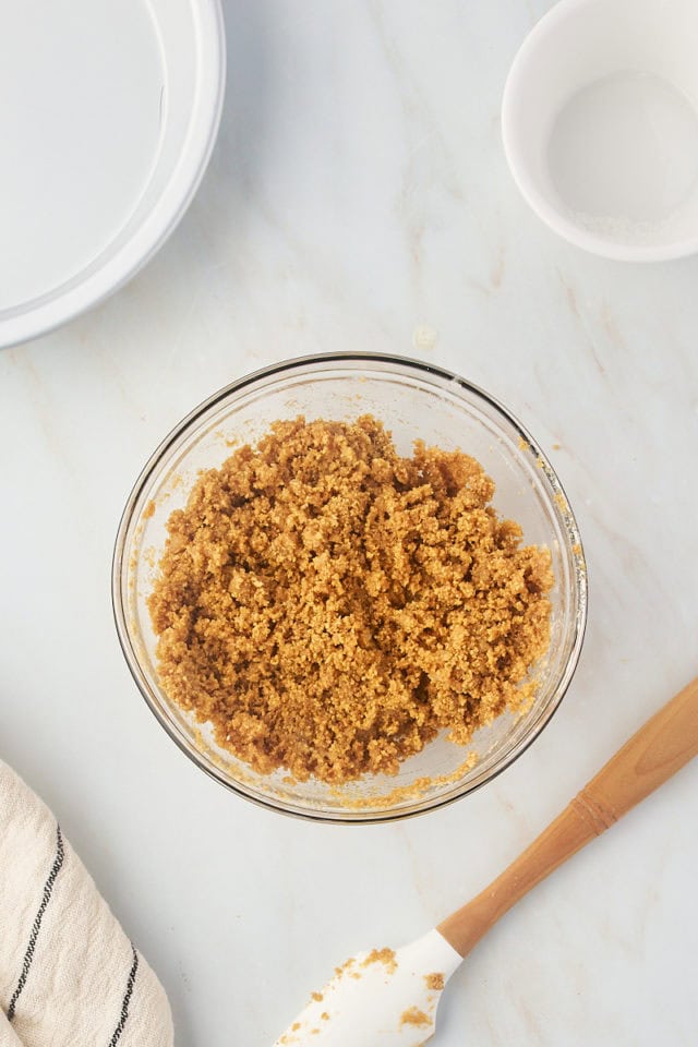 overhead view of graham cracker crust mixture in a glass mixing bowl